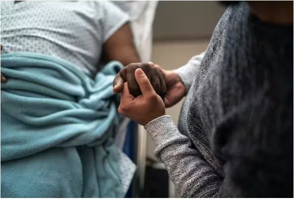 فردی که دست بیمار را در تخت بیمارستان دراز کشیده است